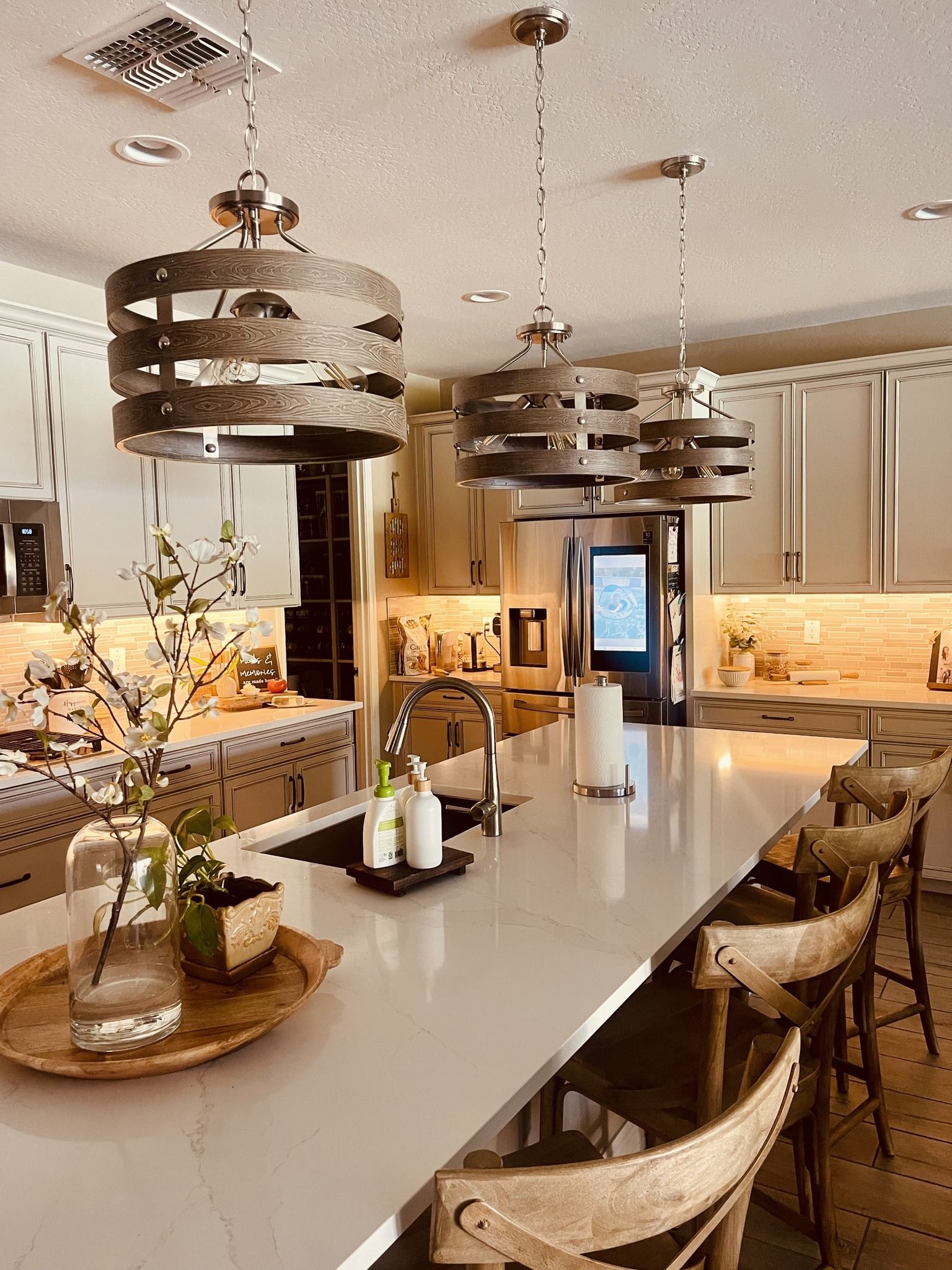 Kitchen with white countertops, three pendant lights, and wooden bar stools.