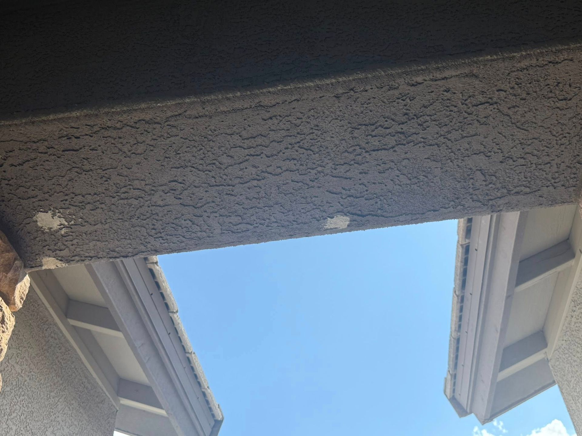 Looking upwards, a sky view through a stucco covered opening. Patches of white appear on the ceiling.