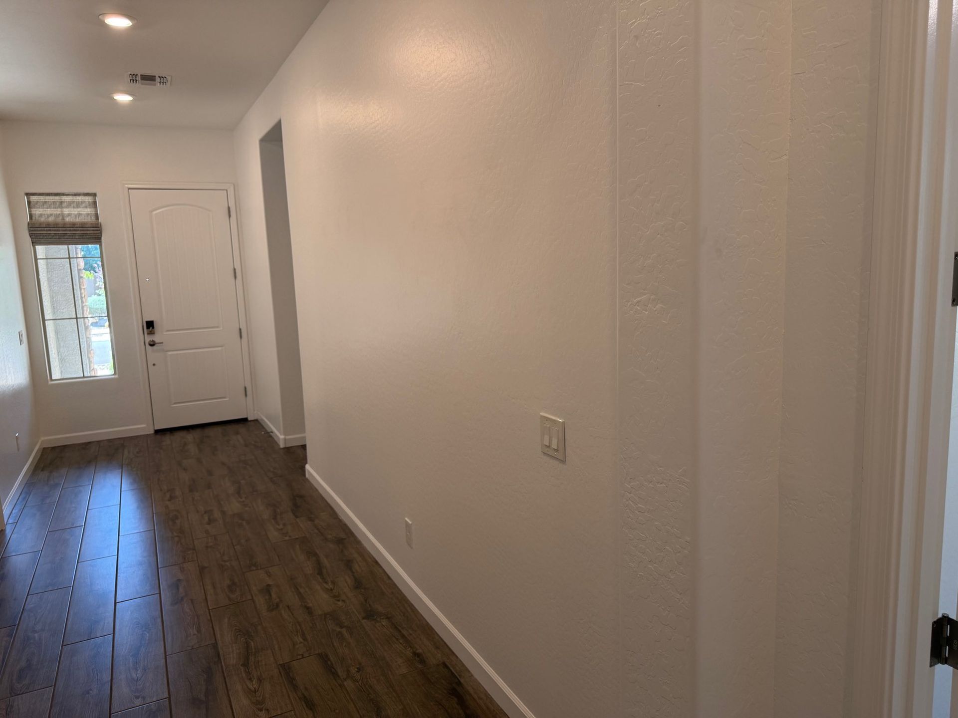Hallway with wood-look floor, white walls, door, and window with blinds.