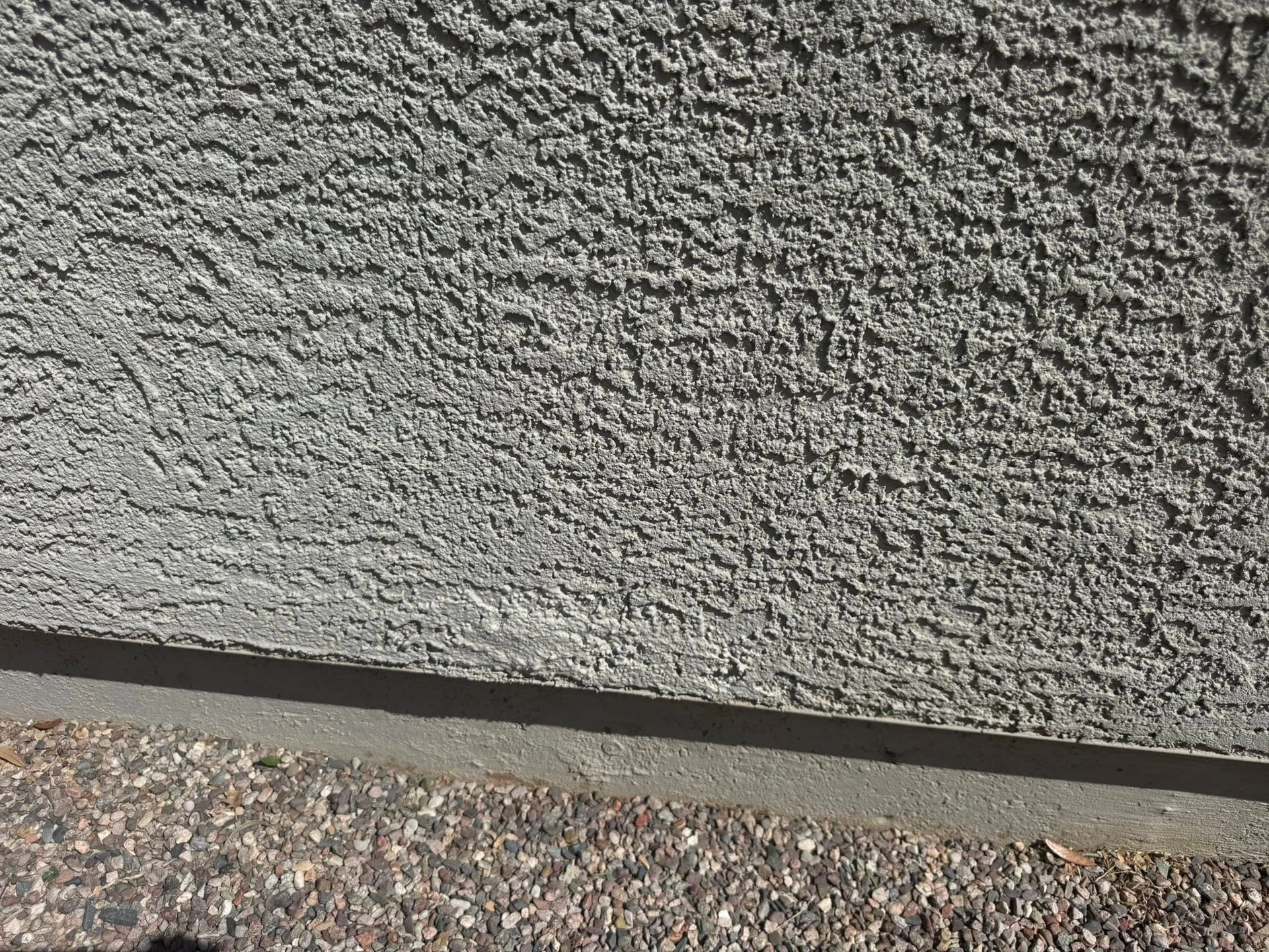 Textured stucco wall with a concrete base. Gravel surface below.