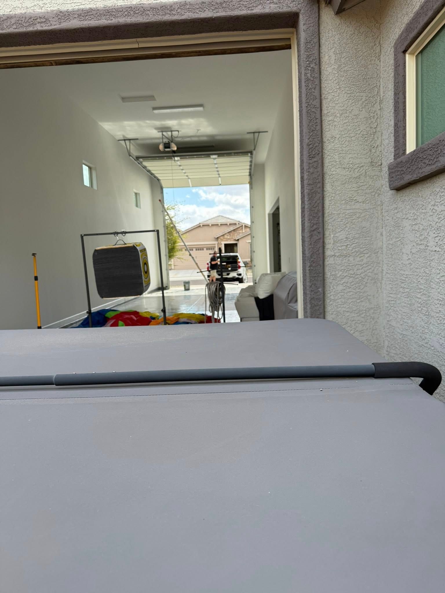 View from a light gray hot tub cover into a breezeway, with items like a net and a car visible.
