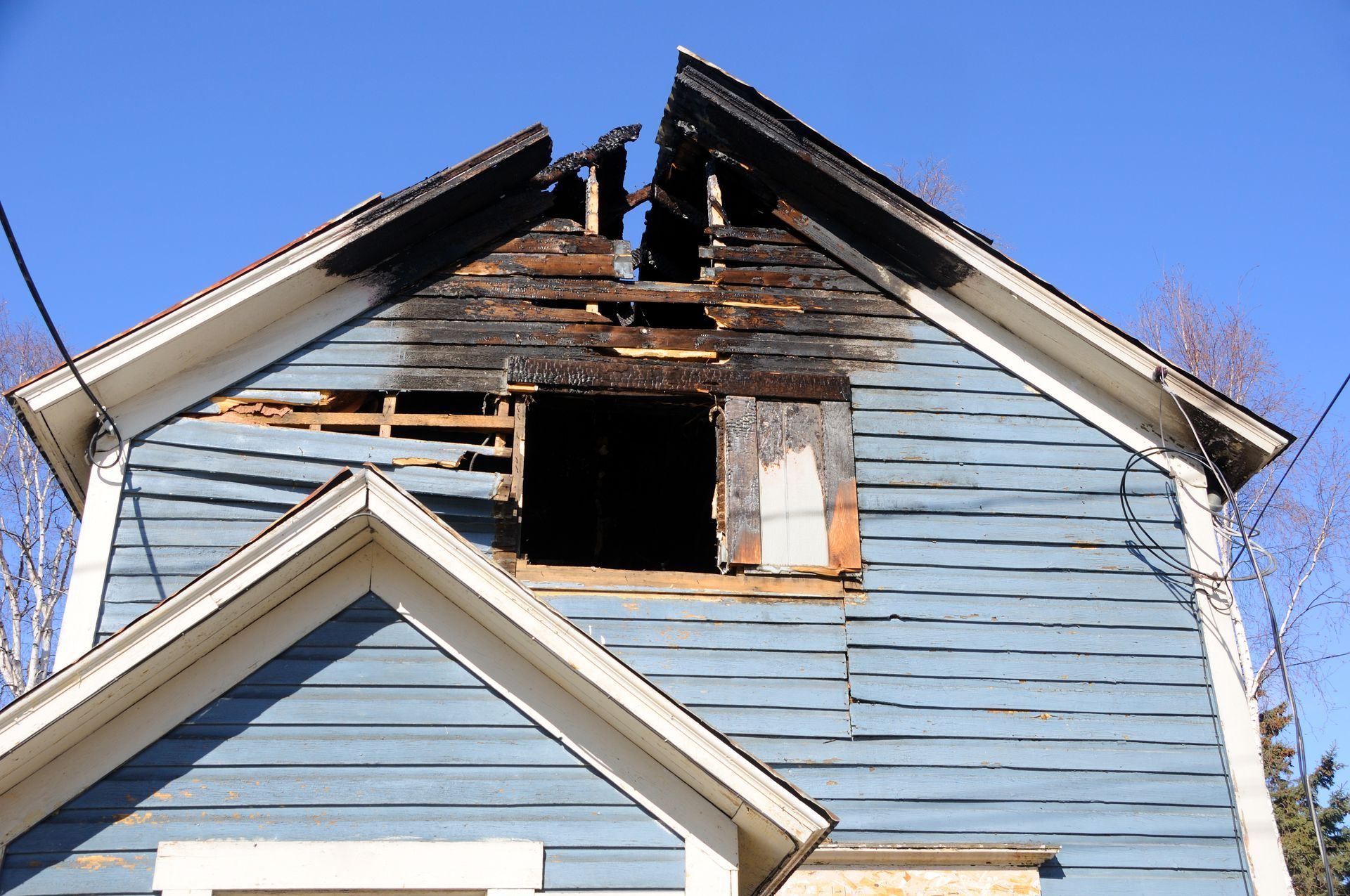 A blue house with a broken roof and a broken window