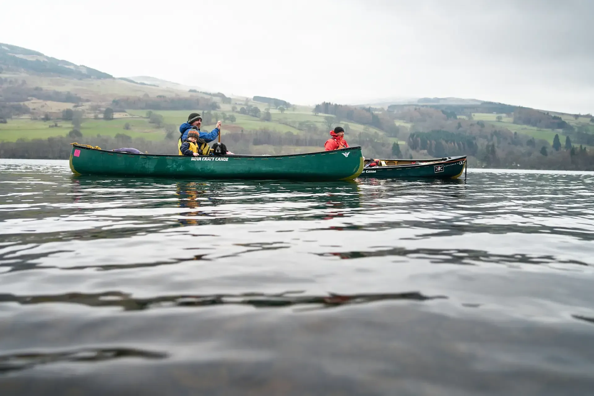 Two canoes on a lake with people paddling; mountains in the background under a cloudy sky.