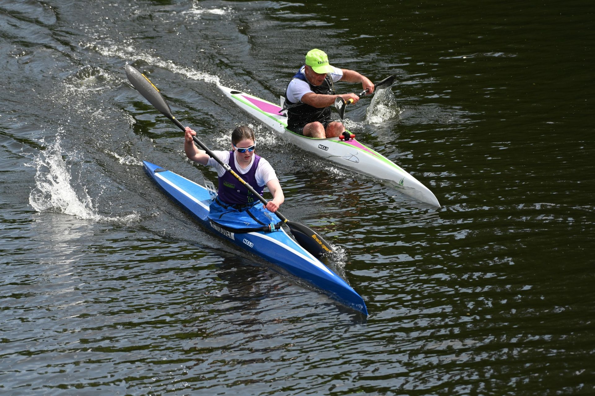 Three kayakers in white kayaks paddle through choppy water under a blue sky.