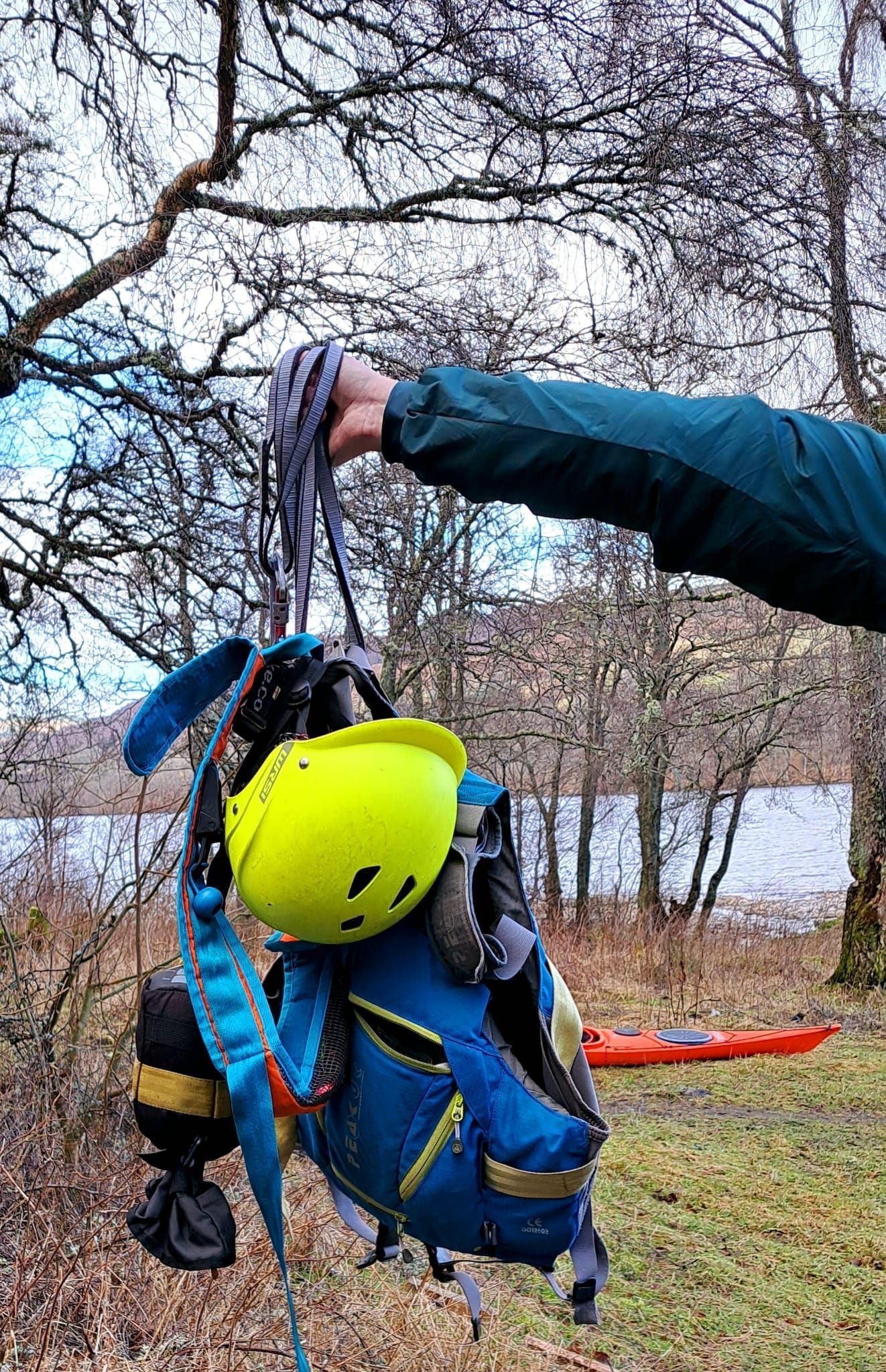 A person is holding a backpack with a helmet and a kayak on it.