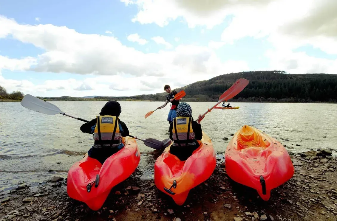 Three people in kayaks on the shore of a lake