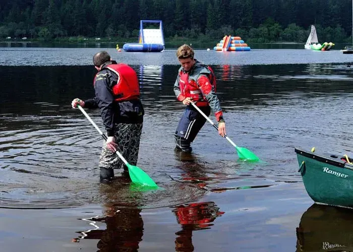 Two men are standing in the water with oars in their hands