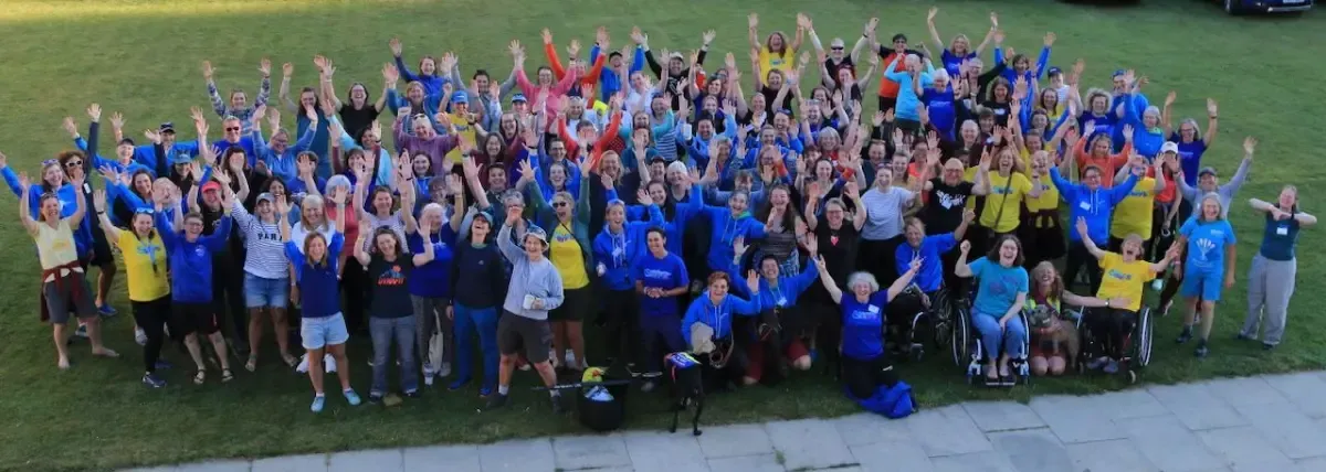 Large group of people with arms raised in a field; most wearing blue, some in wheelchairs.