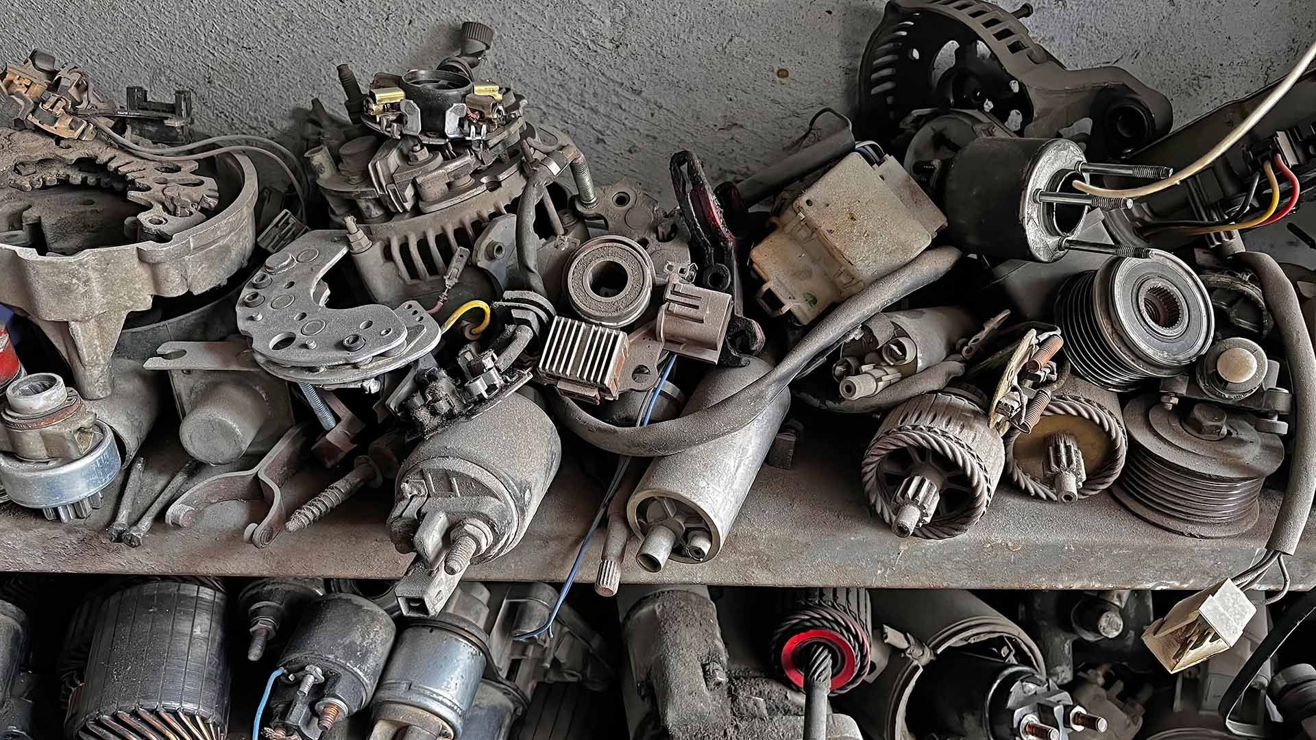 Shelves of used car alternators, starters, and metal auto parts in a workshop.