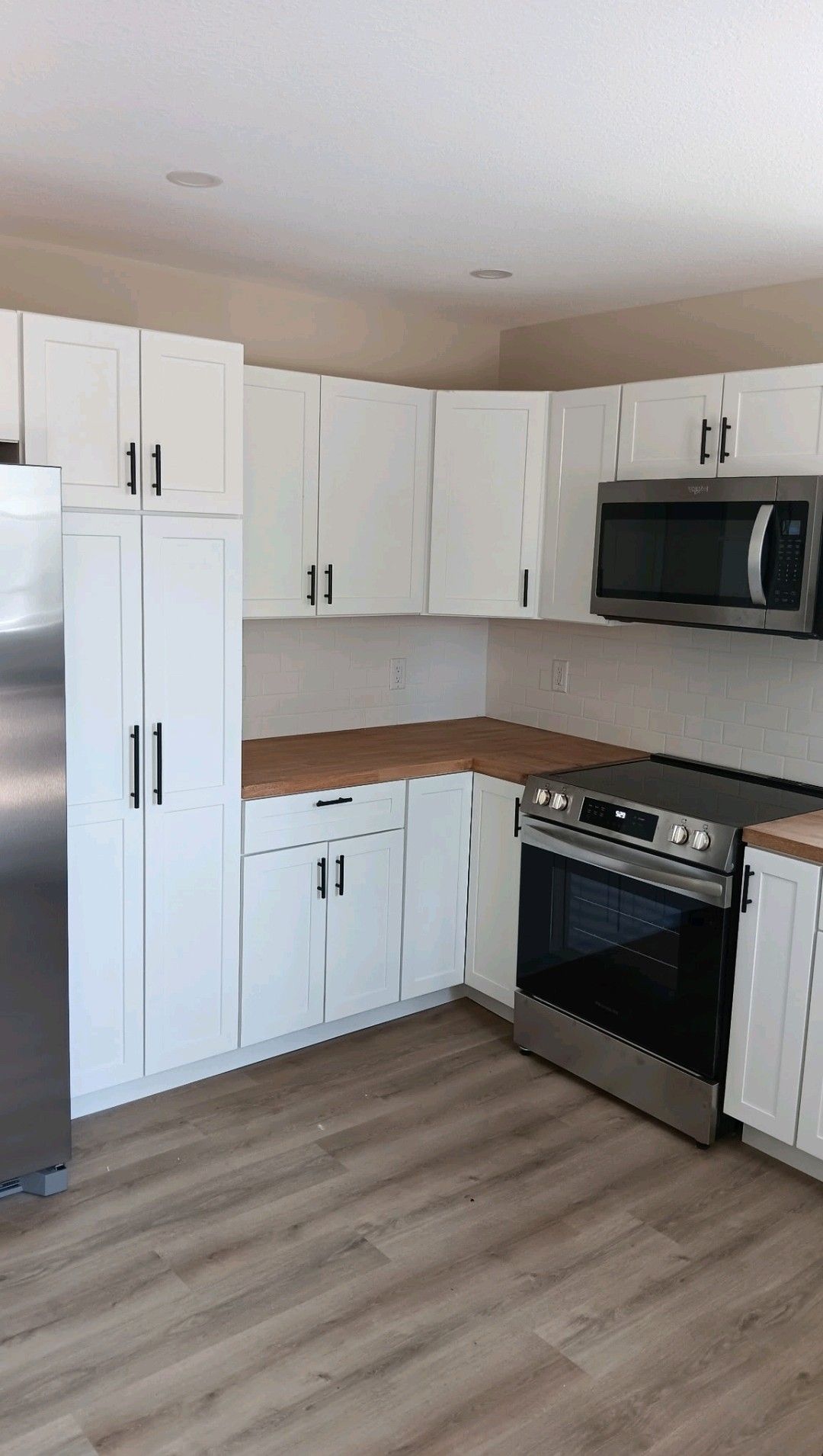 Modern kitchen with white cabinets, wood countertops, stainless fridge, oven, and microwave