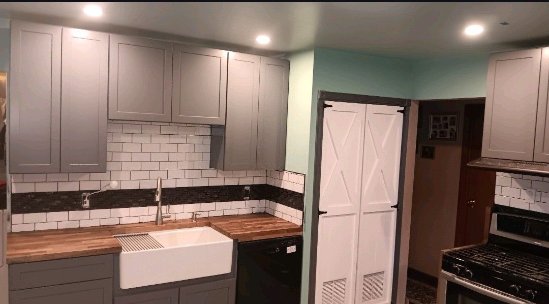 Modern kitchen with gray cabinets, white subway tile, farmhouse sink, and stainless stove under recessed lights