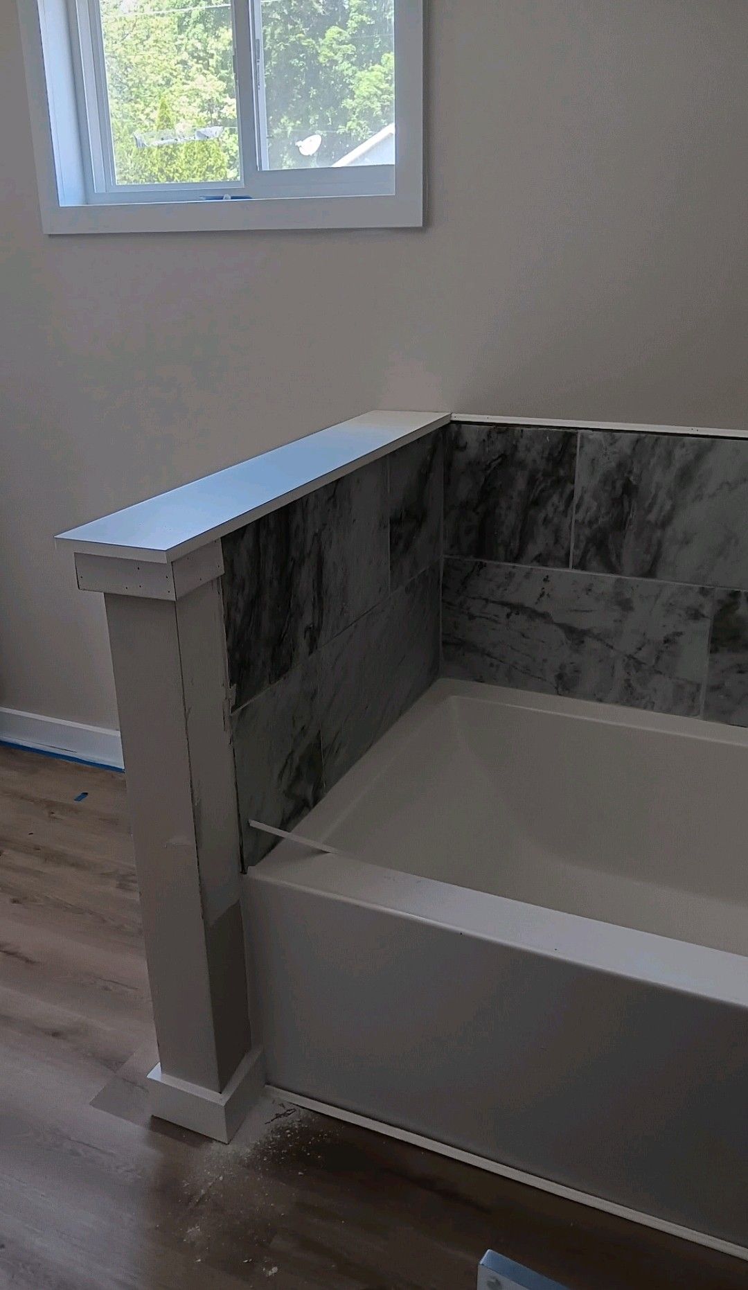 A marble-accented bathtub by a window in a bright bathroom.