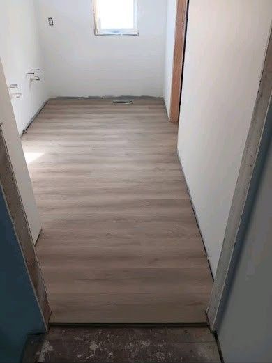 Narrow empty hallway with light wood flooring and a small window at the far end.