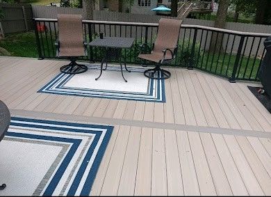 Outdoor deck with two chairs and a small table on blue-and-white rugs, bordered by black railing.