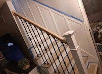 Interior staircase with wooden handrail and white paneled wall, viewed at a diagonal angle