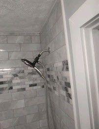 Tile shower corner with a chrome showerhead and white door frame.