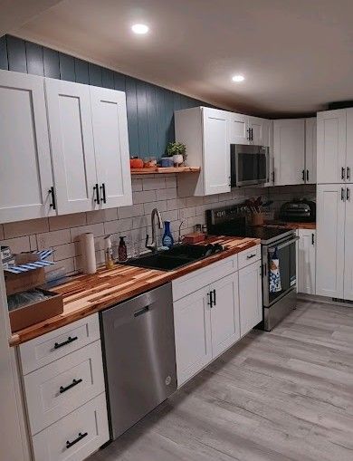 Modern kitchen with white cabinets, wood countertops, stainless appliances, and gray flooring