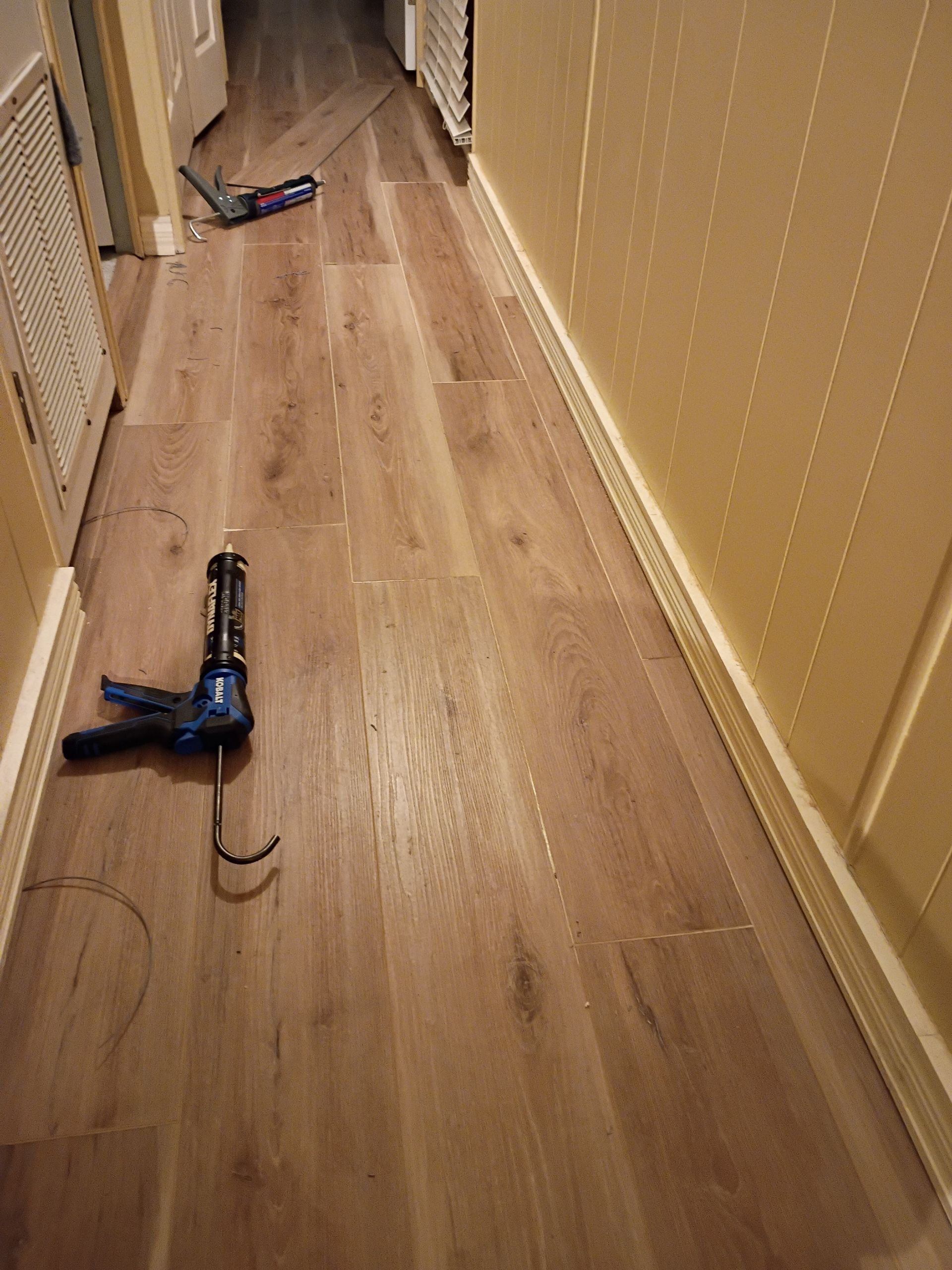 Hallway with wood floor and yellow walls, two cordless drills lying on the floor, one in the foreground
