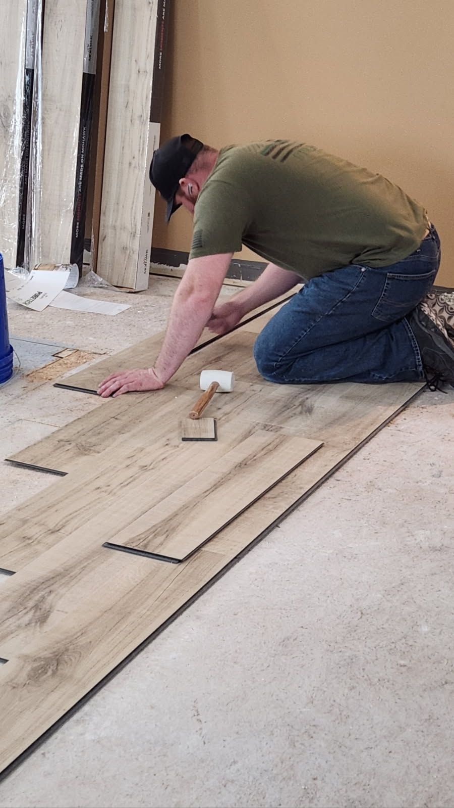 Man kneeling on floor installing wood planks in a room under renovation