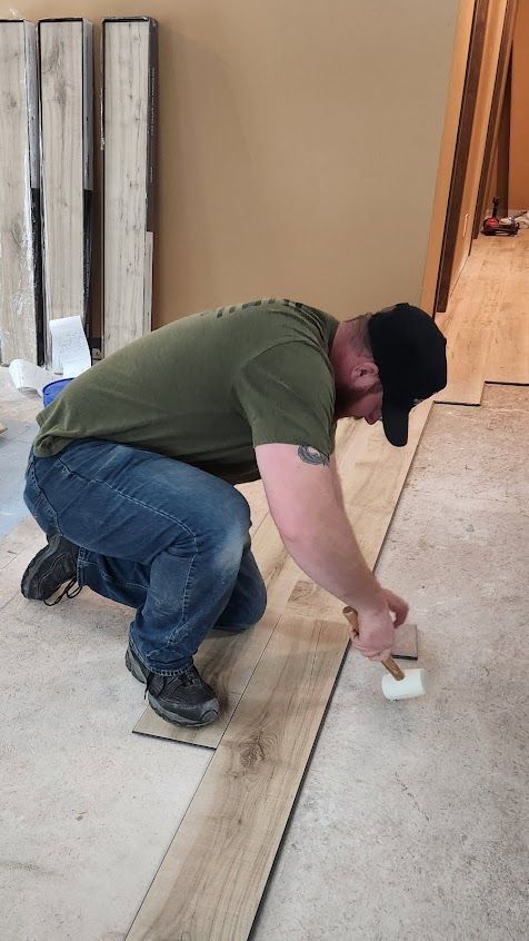 Worker kneeling on a floor, using a small trowel to spread material along a wood plank seam
