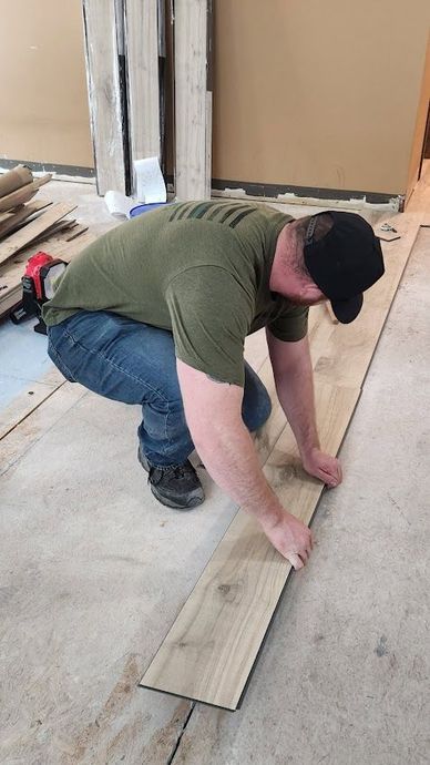 Worker kneels on a concrete floor, aligning wood flooring planks during installation.