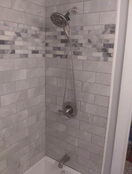 Tiled shower with chrome showerhead, handheld spray, and tub spout in a gray bathroom.