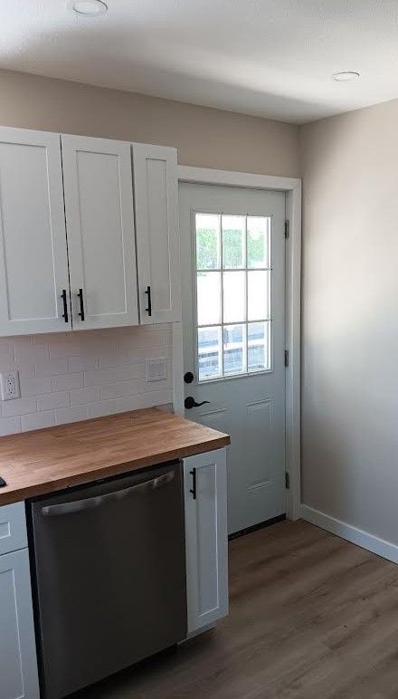 Small kitchen with white cabinets, wood countertop, stainless dishwasher, and a glass-paned back door.