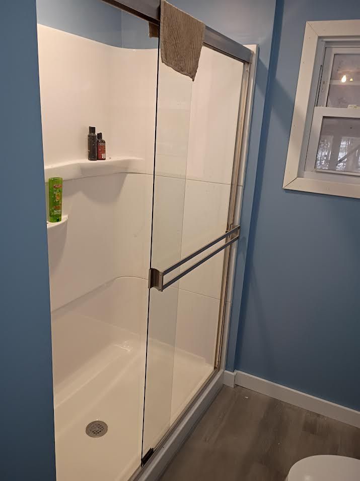 Bathroom shower with clear glass door, white tile, and blue wall beside it.
