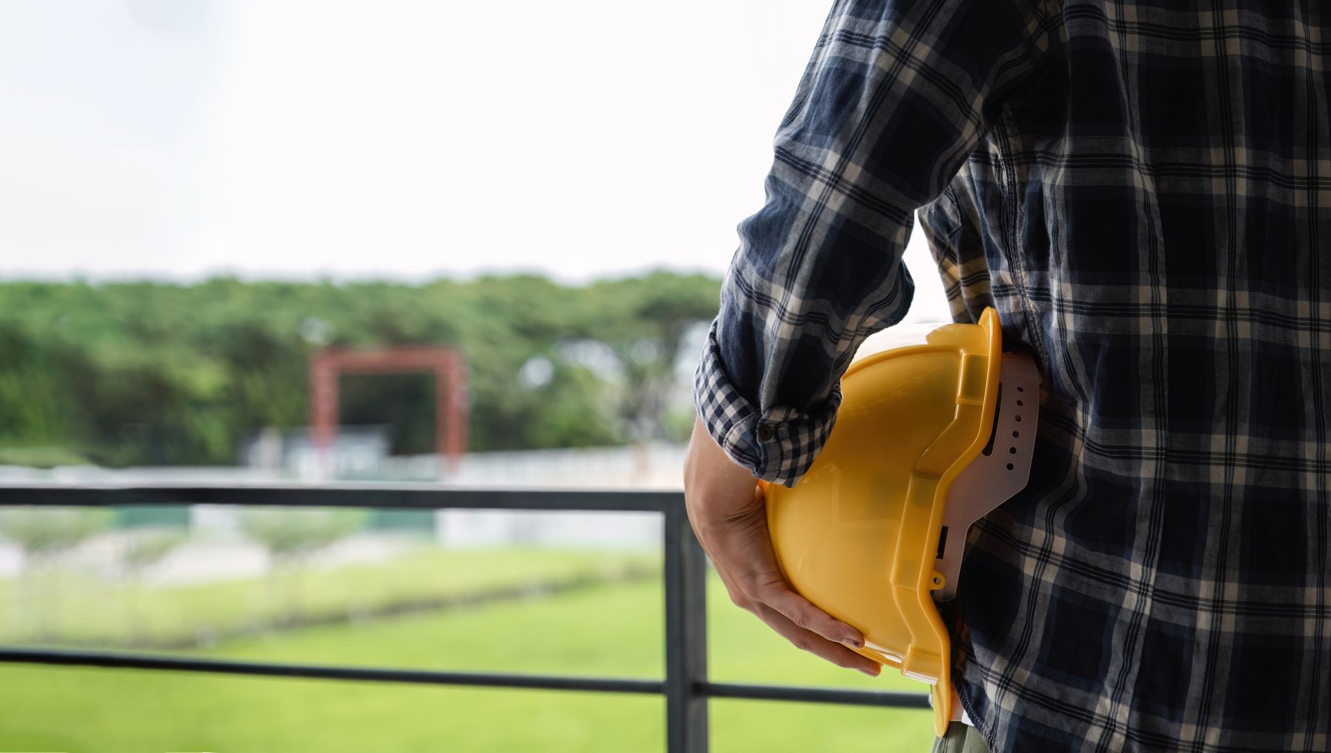 Male commercial general contractor standing holding safety helmet looking out at construction site.
