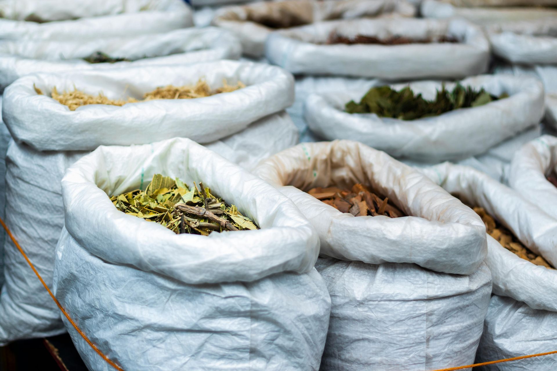 White sacks filled with dried leaves or herbs stacked outdoors