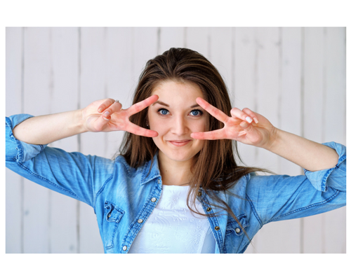 A woman in a denim shirt is making a peace sign with her hands.