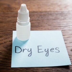 A bottle of eye drops is sitting on a piece of paper that says dry eyes.