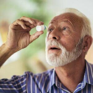 A man with a beard is applying eye drops to his eye.