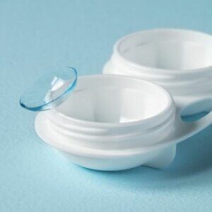 A pair of contact lenses in a white container on a blue surface.