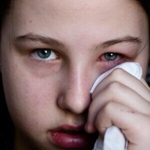 A young girl is wiping her eyes with a napkin.