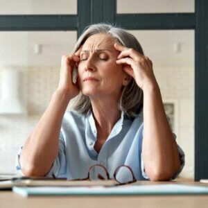 A woman is sitting at a table with her hands on her head.