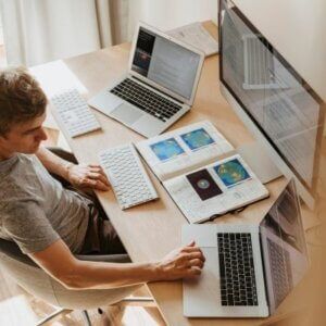 A man is sitting at a desk with two laptops and a computer.