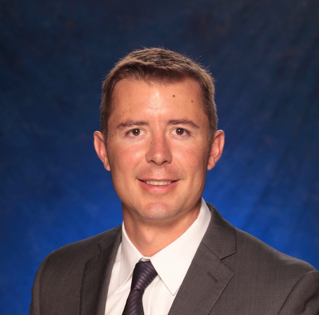 A man in a suit and tie is smiling in front of a blue background