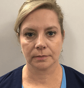 A woman in a blue scrub top is looking at the camera.