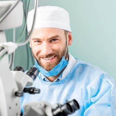 A surgeon is smiling while looking through a microscope in an operating room.