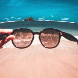 Sunglasses being held on a beach showing the difference they make in eye comfort.