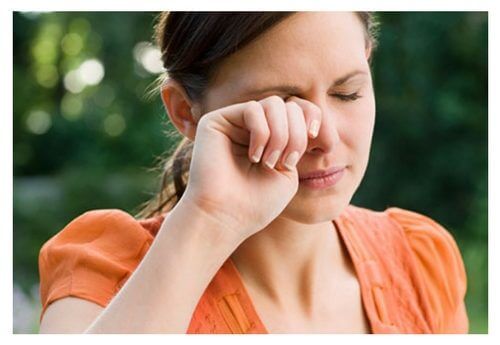young woman outside dealing with eyelid itching by rubbing her eye