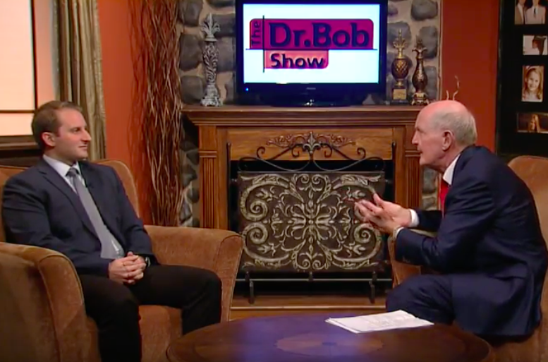 Two men are sitting in front of a tv that says dr bob show