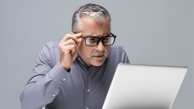 A man wearing glasses is looking at a laptop computer.