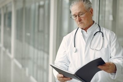 A doctor with a stethoscope around his neck is reading a book.