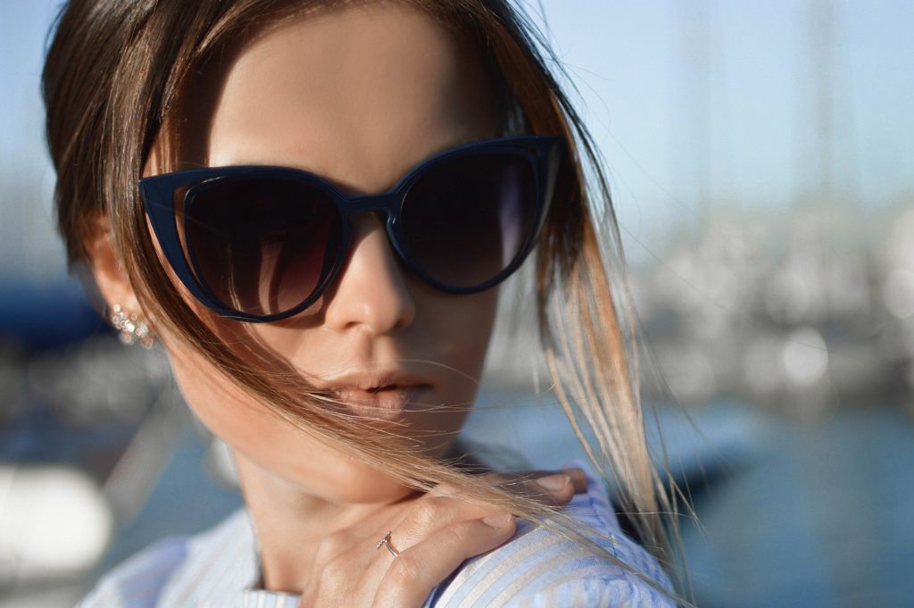 A woman wearing sunglasses with her hair blowing in the wind.