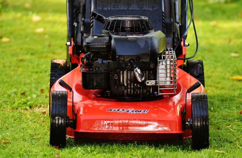 A red lawn mower is sitting on top of a lush green lawn.
