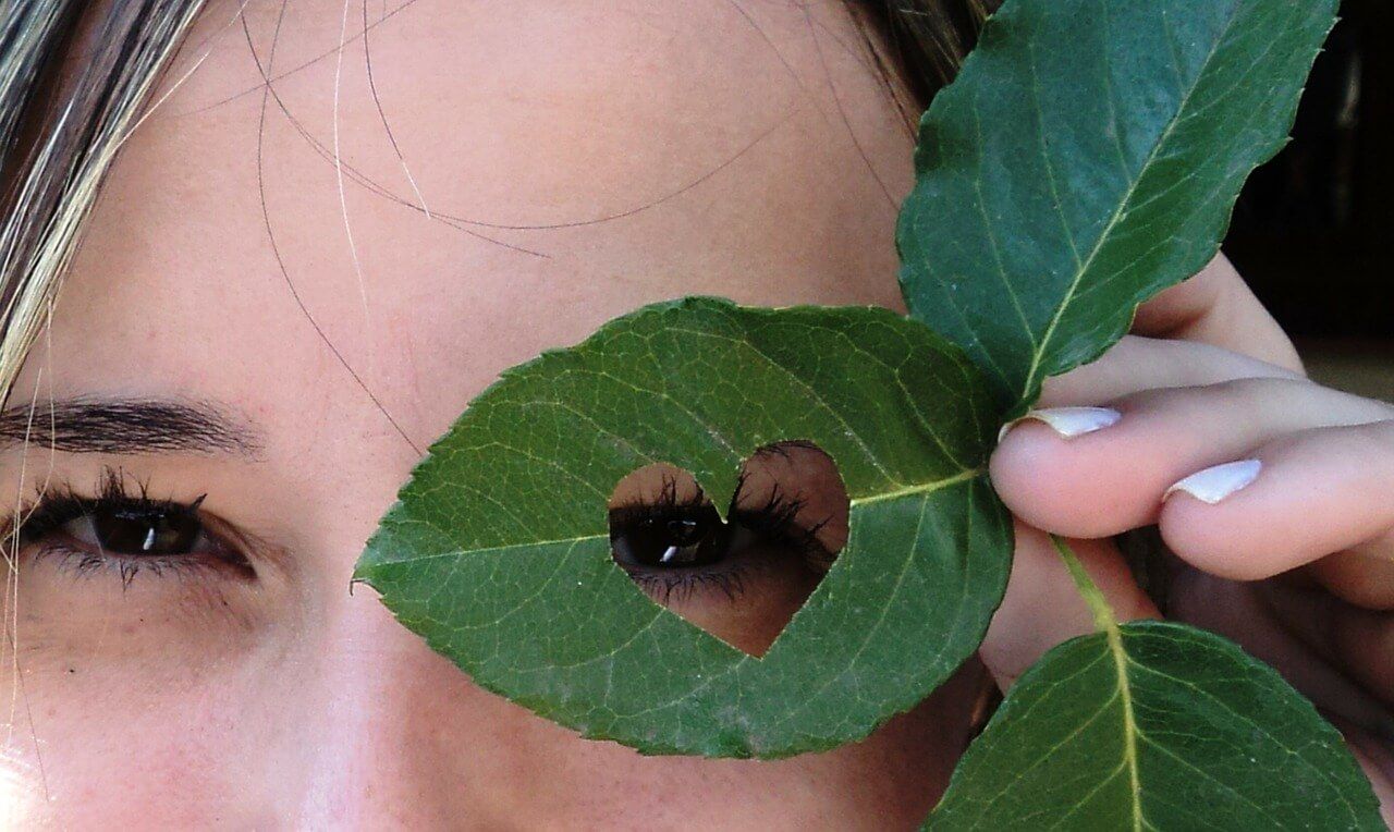 A woman covering her eyes with a leaf with a heart cut out of it