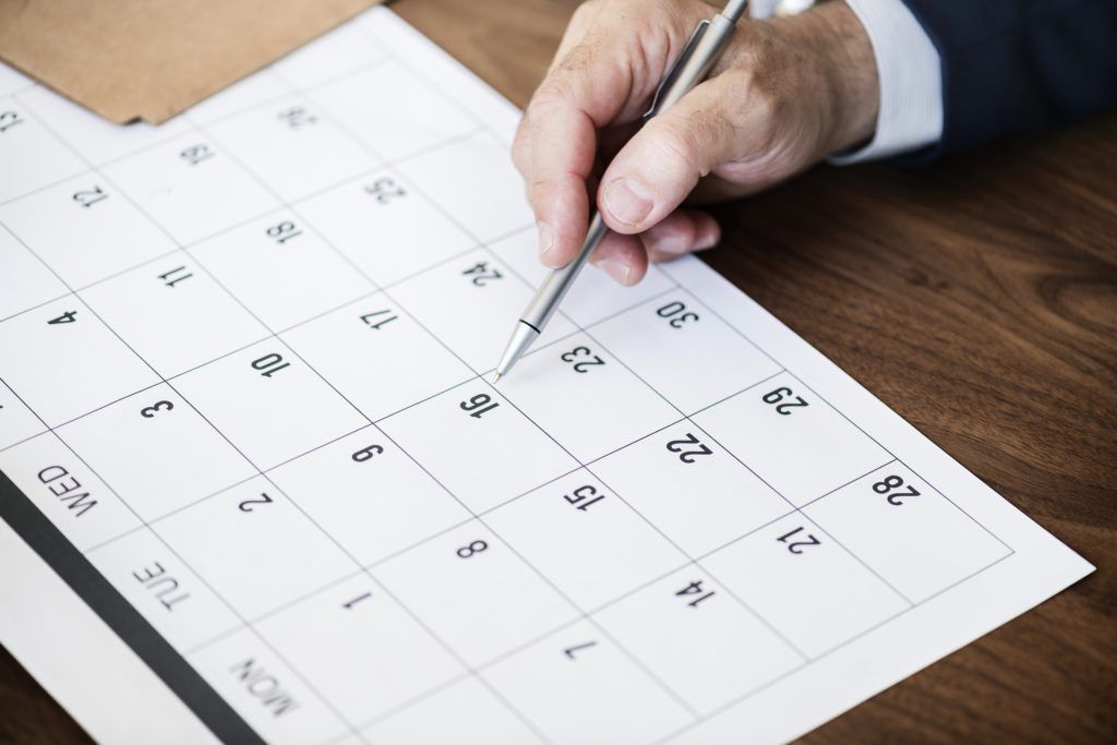 A person is writing on a calendar with a pen.