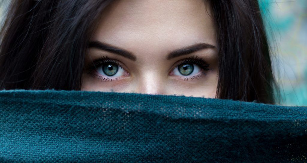 A close up of a woman covering her face with a scarf.